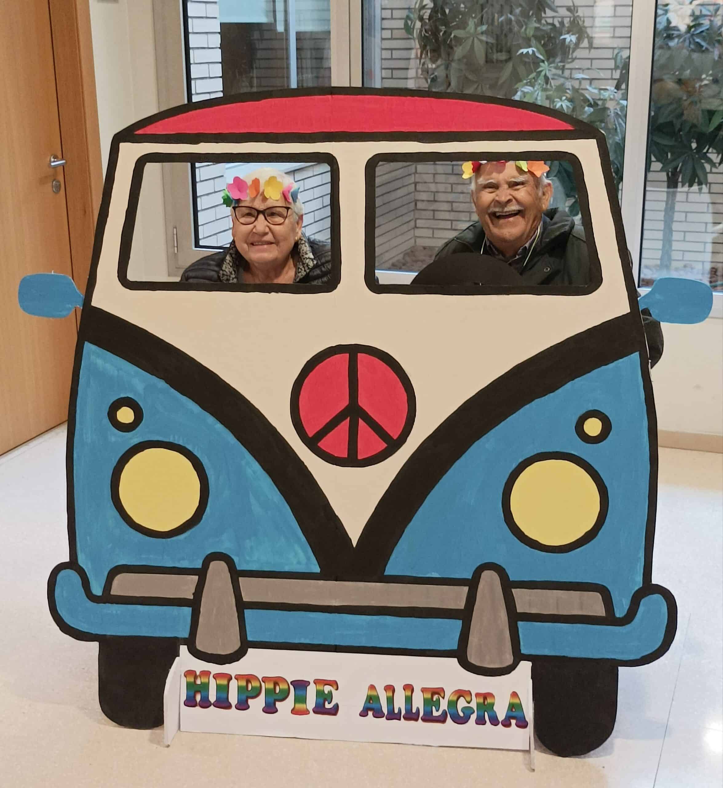 Residentes posan felices ante la cámara tras un photocall de coche hippie confeccionado para la fiesta de Carnaval