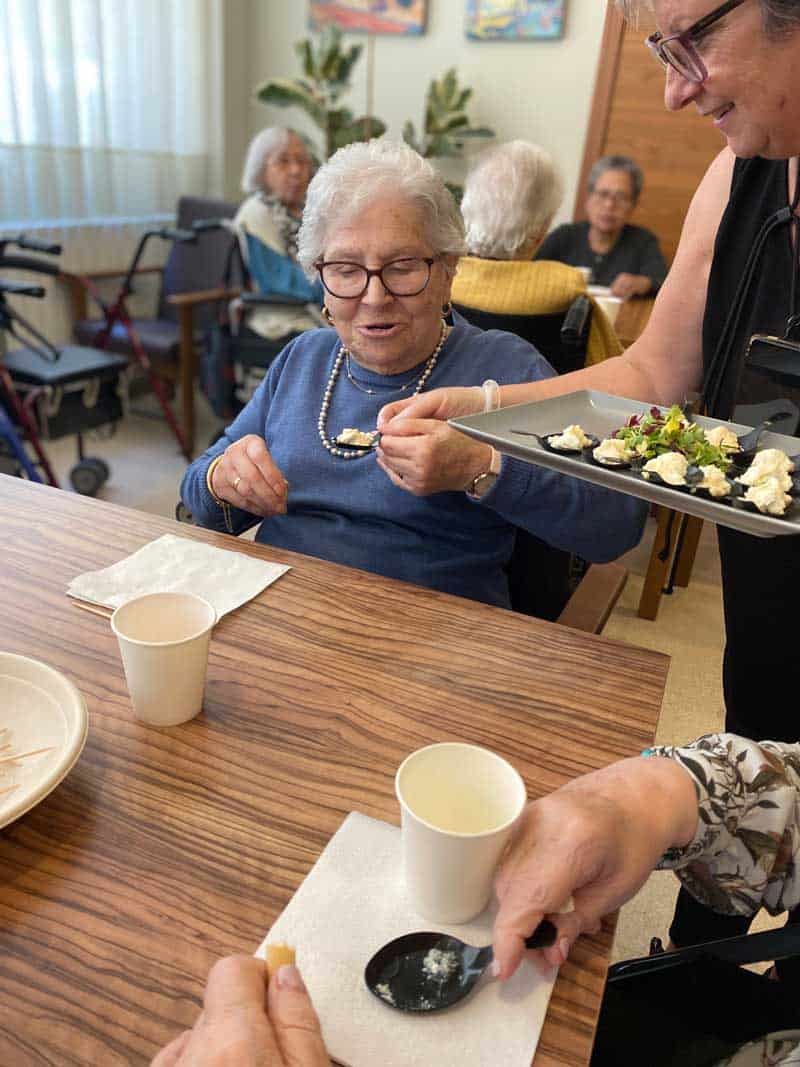 Residente prueba un tipo de queso que le ofrece una cuidadora