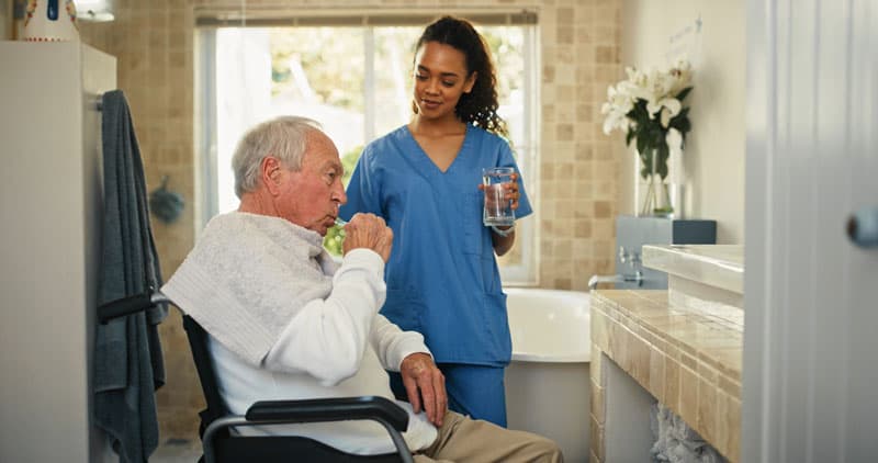 Auxiliar ayuda a un residente a lavarse los dientes