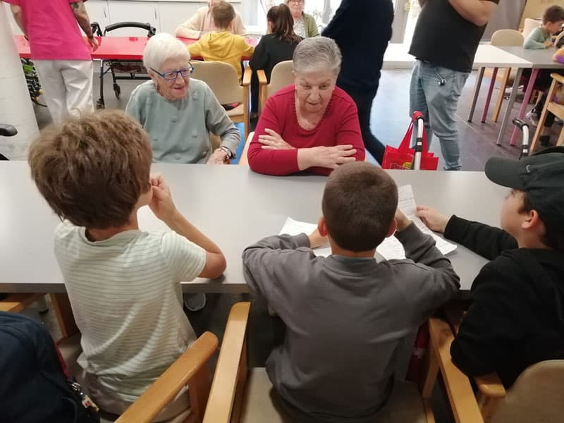 Residentes escuchan con atención las preguntas de los niños en el taller de radio celebrado en Benviure