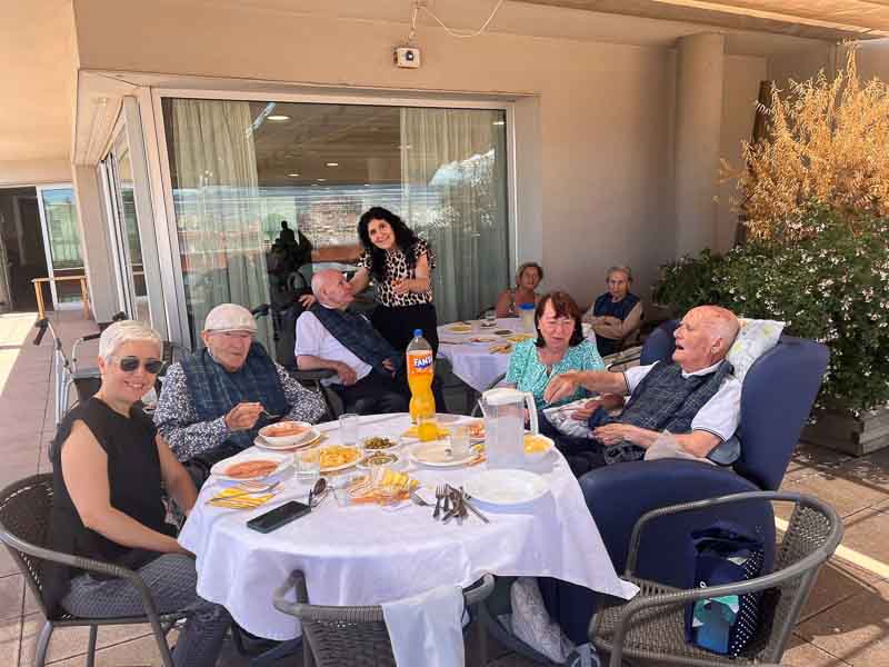 Residentes y familiares posan sonrientes en las mesas mientras comen la paella