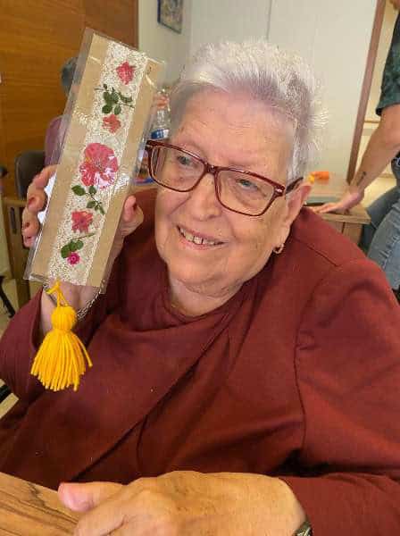 Residente posa sonriente con su punto de libro realizado en un taller junto a familiares