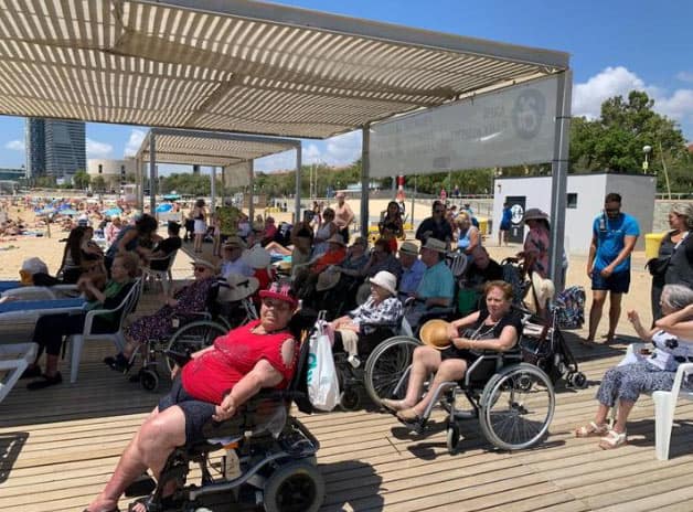 uchos de ellos en silla de ruedas, a la sombra durante su salida a la playa