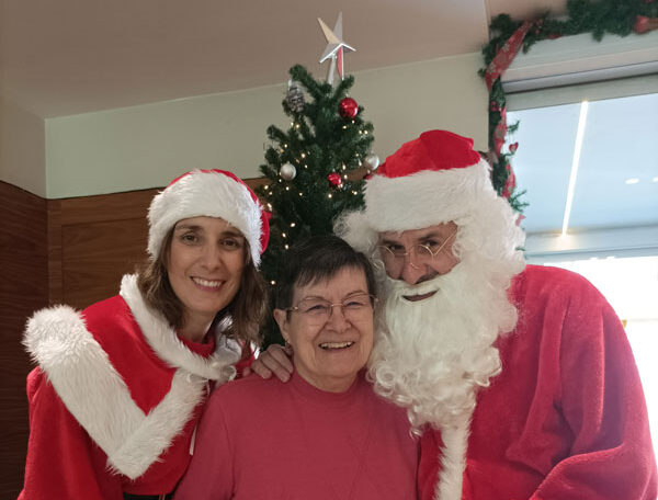 Una residente posa sonriente junto a Papá y Mamá Noel