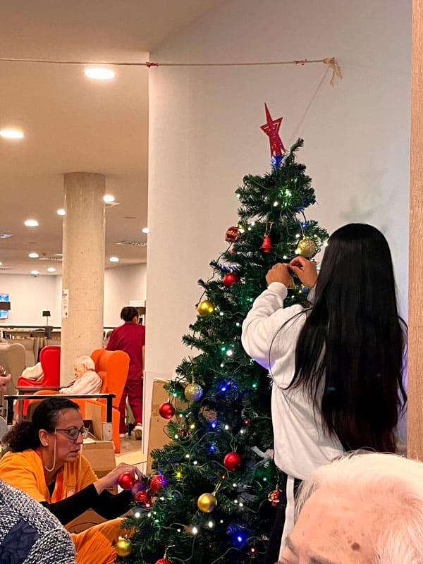 Una auxiliar ayuda a una residente a decorar el árbol de Navidad